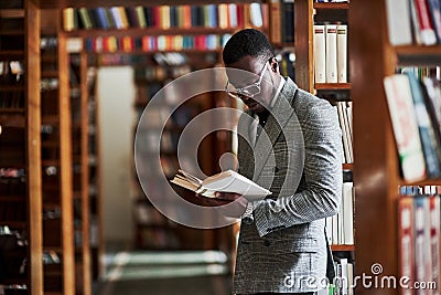 Smart looking african american businessman in glasses standing and reading a book in library Stock Photo