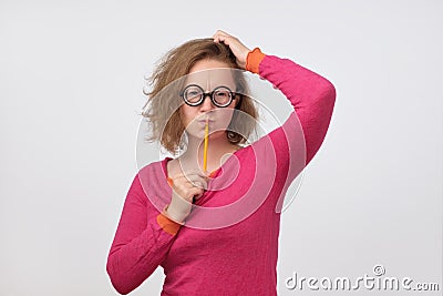 Smart minded woman in funny glasses thinking about excellent idea holding pencil near mouth. Stock Photo