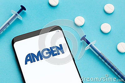Smart phone showing Amgen logo on screen and pills and syringe on blue background Editorial Stock Photo
