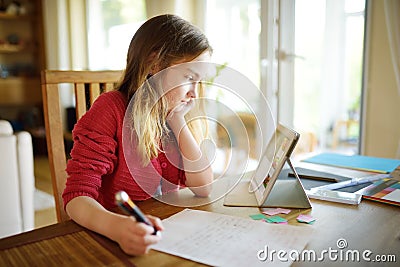 Smart schoolgirl doing her homework with digital tablet at home. Child using gadgets to study. Education and learning for kids. Stock Photo