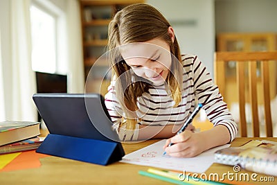 Smart preteen schoolgirl doing her homework with digital tablet at home. Education and distance learning for kids. Homeschooling Stock Photo