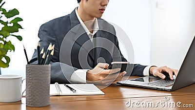 Smart Asian male banker working at his office desk, using smartphone and laptop Stock Photo