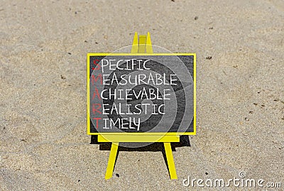 SMART symbol. Concept words SMART specific measurable achievable realistic timely on blackboard. Beautiful sand background. Stock Photo