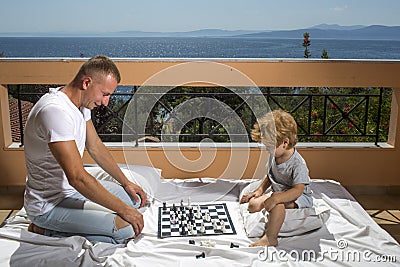 Smart toddler concept Dad with child play intellectual game Father and little son play chess on balcony nature and sea Stock Photo