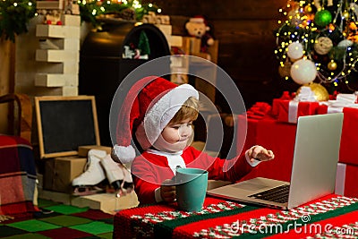 Smart toddler surfing internet. Little boy santa hat and costume. Boy child with laptop near christmas tree. Buy Stock Photo