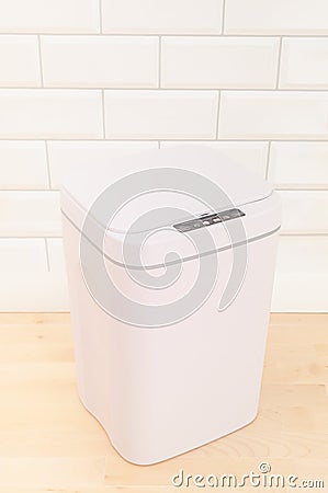 Smart waste basket. Electronic gadget for the home. The cover is closed. On a wooden floor. White tile background. View from above Stock Photo