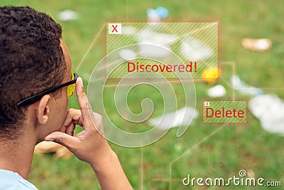 Smart Waste Sorting. African boy wearing digital glasses sitting in the park looking at grass pensive using app for Stock Photo