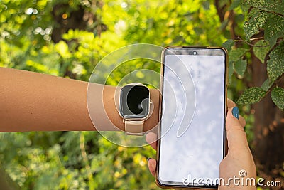 smart watch and a phone with a white screen in the hands of a girl in the park, new technologies and people, a watch Stock Photo