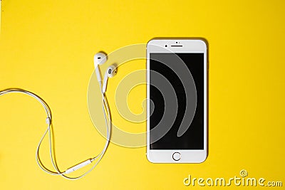 Smartphone with Blank Screen Connects to Earphones with Spiral Cable on yellow Background Top View Stock Photo