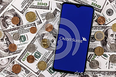 Smartphone with Credit Suisse bank logo surrounded by variety of metal coins on background of dollar bills Editorial Stock Photo