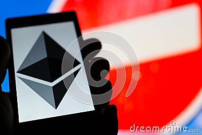 Smartphone in hand with Etherium cryptocurrency logo. Prohibiting red sign on background. Banned money concept. Censorship. Editorial Stock Photo