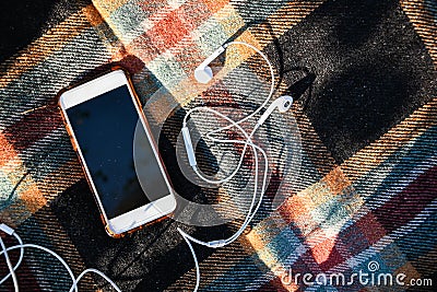 Smartphone with headphones on the cozy sweaters. Top view. Autumn flatlay. Outdoor listening podcasts Stock Photo