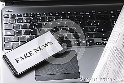 Smartphone with the phrase fake news written on the screen on a laptop, newspaper and magnifying glass Stock Photo