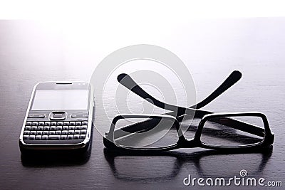 Smartphone with qwerty keypad and pair of eyeglasses Stock Photo