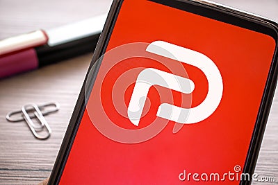 Smartphone with red parler logo on wooden table. Phone concept social media platform icon on display screen Editorial Stock Photo