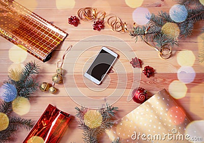 Smartphone surrounded by fir branches, wrapping paper`s rolls and christmas decorations. Preparation for holidays Stock Photo