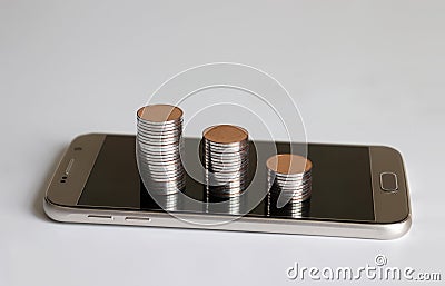 Smartphone and three piles of coins. Stock Photo