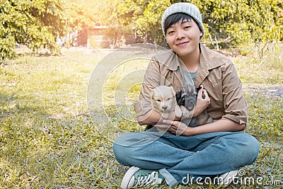 Smile Asian owner carrying, hugging adorable puppy dog on her sitting green grass backyard lawn Stock Photo