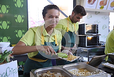 Smile female seller putting some frog chips on a plastic plate Editorial Stock Photo