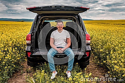 Smiled young man sitting in the trunk of a car Stock Photo