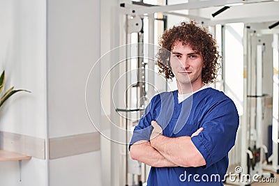 Smiled young physical therapist standing arms crossed while working at the rehabilitation centre Stock Photo