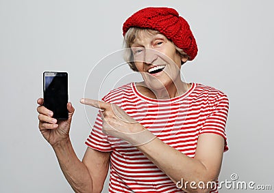 Smiley senior woman is holding a new smartphone in her hand. She has learned how to use it. Stock Photo
