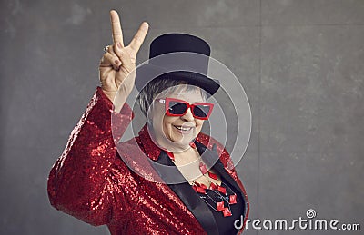 Happy senior woman in sequin outfit, top hat and cool glasses doing V sign gesture Stock Photo
