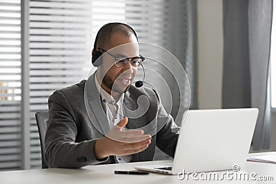 Smiling African American employee in headset using laptop, talking online Stock Photo