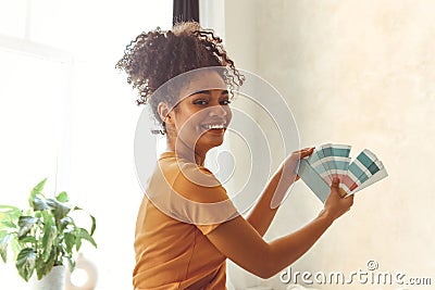 Smiling African American girl stands back to camera in middle of bed room with palette of blue shades for interior renovation Stock Photo