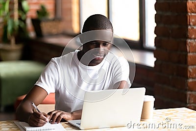 Smiling black male studying on laptop making notes in notebook Stock Photo