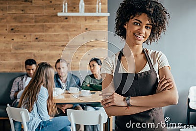 Smiling african american waitress standing with customers sitting behind Stock Photo