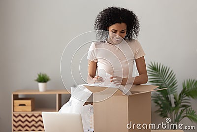 Smiling African American woman unpacking parcel, removing bubble wrap Stock Photo