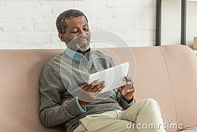 smiling african anerican man using laptop while sitting on sofa. Stock Photo