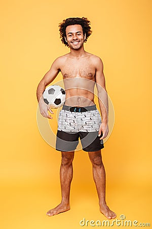 Smiling african man in summer shorts standing and holding football Stock Photo