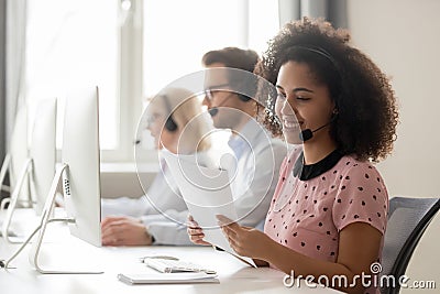 Smiling african woman call center operator wearing headset reading papers Stock Photo