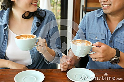 Smiling Asian couple in blue jean shirt having hot heart latte art coffee Stock Photo