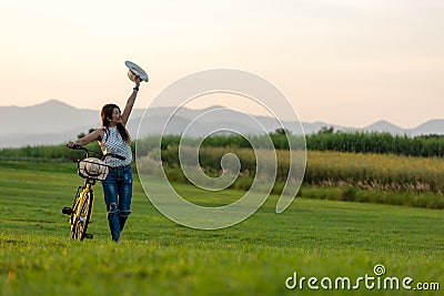 Smiling Asia woman with bicycling at the garden meadow in sunset near mountain background. Stock Photo