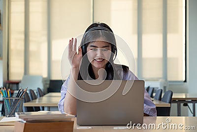 Smiling Asian girl in headphones have video call distant class with teacher using laptop, happy small child wave Stock Photo