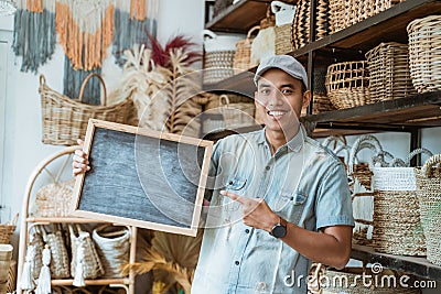 smiling Asian man looking at the camera and finger pointing to blackboard in a handicraft shop Stock Photo