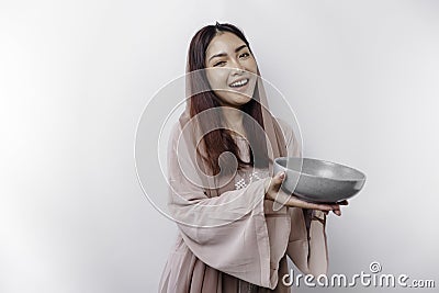 A smiling Asian Muslim woman is fasting and hungry and holding and pointing to a bowl Stock Photo