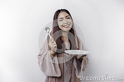 A smiling Asian Muslim woman is fasting and hungry and holding and pointing to a plate Stock Photo