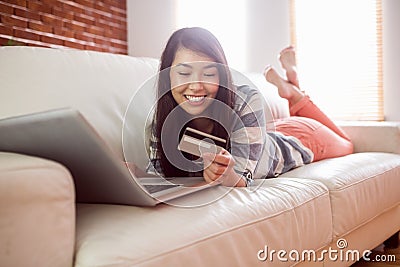 Smiling asian woman on couch using tablet to shop online Stock Photo