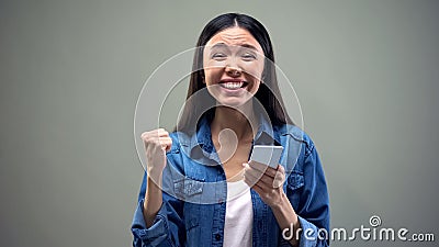 Smiling asian woman with smartphone doing yes gesture, giveaway winner, luck Stock Photo