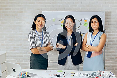 Smiling Asian young business women in casual wear standing in line with arms folded in meeting room Stock Photo