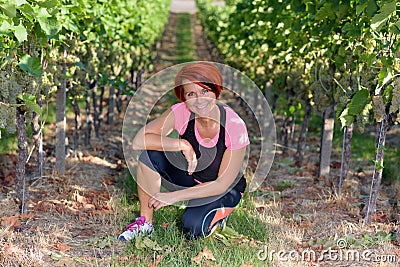 Smiling athletic woman kneeling in a vineyard Stock Photo