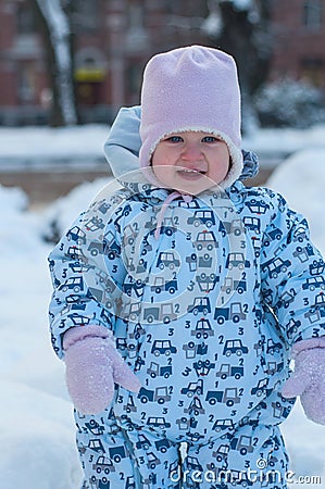 Smiling baby in blue overall, pink hat and mittens. people, children and winter concept. Portrait of a little girl in winter cloth Stock Photo