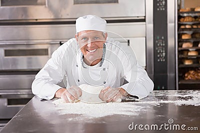 Smiling baker kneading dough on counter Stock Photo