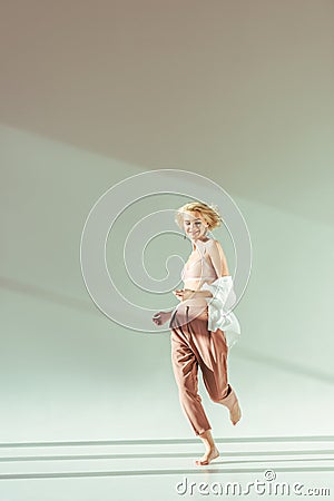 smiling barefoot blonde woman in pink bra, shirt and pants running Stock Photo