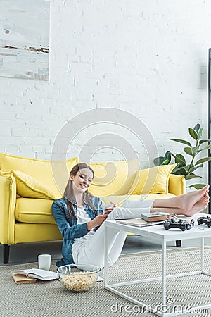 smiling barefoot girl sitting on carpet and using smartphone while studying Stock Photo