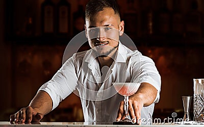 Smiling bartender gives the guest a chic cocktail in a tall glass. Stock Photo